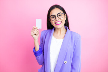 Young business woman wearing purple jacket over pink background smiling and holding white card