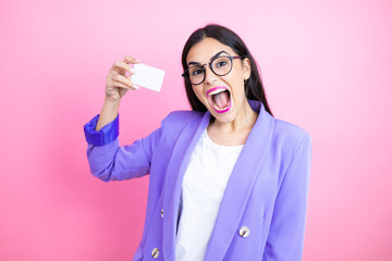 Young business woman wearing purple jacket over pink background smiling and holding white card