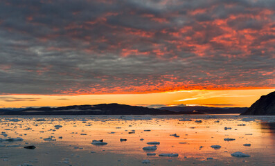 Fototapeta na wymiar Sunset over fjord with icebergs close to Eqip Glacier in Greenland, Danish Territory.