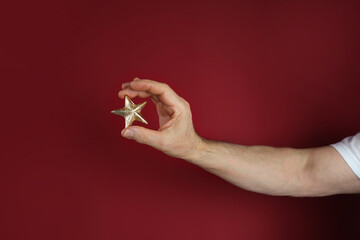 male hand holding gold foil star on red background, concept of evaluating the result, rating, Satisfaction