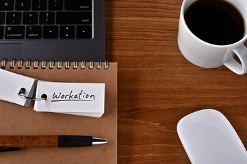 On the desk there is a laptop, a cup of coffee, and a word book with the word Workation written on it.