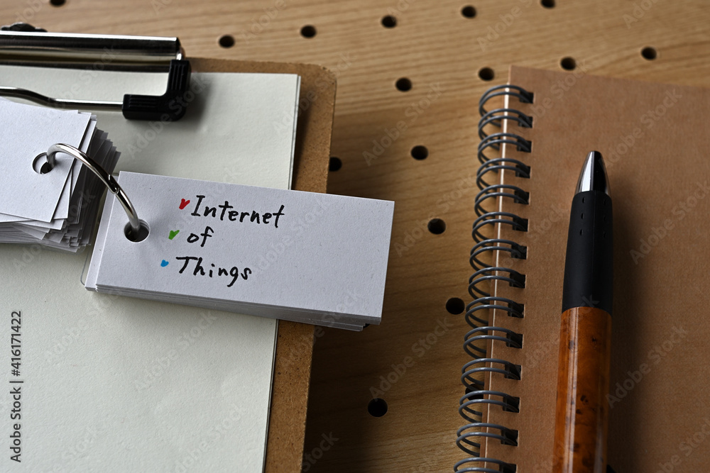 Poster there is a notebook, a pen, and a clipboard with a sticky note stuck to it that says iot written on 
