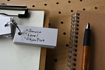 There is a notebook, a pen, and a clipboard with a sticky note stuck to it that says SLO written on...