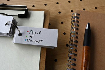 There is a notebook, a pen, and a clipboard with a sticky note stuck to it that says PoC written on...