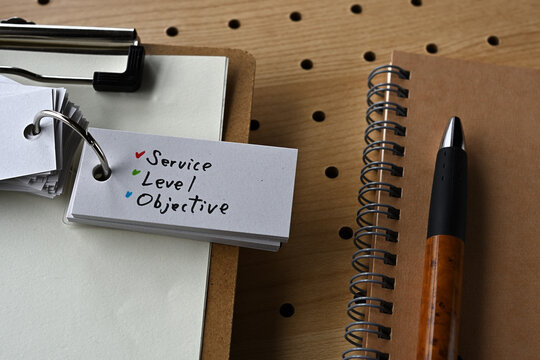 There is a notebook, a pen, and a clipboard with a sticky note stuck to it that says SLO written on it. It was an abbreviation for Service Level Objective.