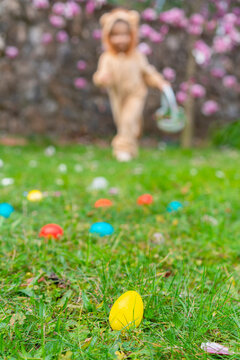 Cute cheerful child in a lion costume looking for and gathering easter eggs in the backyard lawn or park. Easter eggs hunt on spring meadow. Blurred kid's silhouettes with basket. 