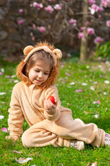 Cute cheerful child in a lion costume looking for and gathering easter eggs in the backyard lawn or park. Easter eggs hunt on spring meadow. Blurred kid's silhouettes with basket. 