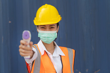 Asian woman worker in mask face and using measures temperature with a non-contact infrared...