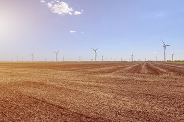 Wind turbines generating electricity on the foreground plowed field. The concept of alternative green energy.