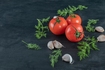 Three fresh tomatoes with leaves on a dark background