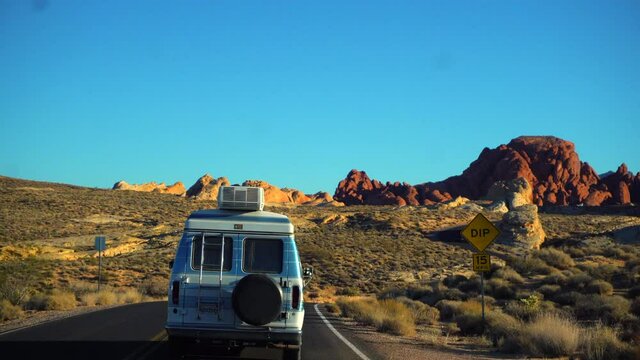 A camper van travels through the valley of fire along the twisting roads. Rocks emulating fire perched in the background create an aura of a different planet.