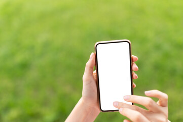 Female hands holding smart phone against blurred green background. Using smartphone mockup