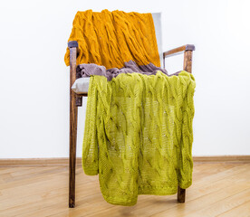 Knitted cotton blanket lies on a wooden chair against a white wall