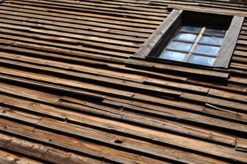 An old, rustic, dark-textured wooden wall and window are captured at a slanted angle to add depth and perspective