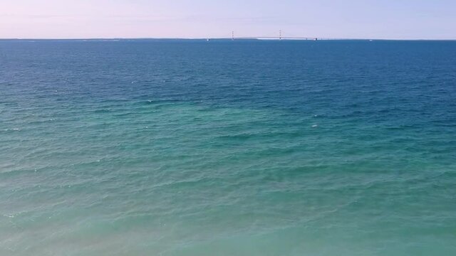Drone view of the blue waters of the Great Lakes near Mackinac island with Mackinac bridge visible in the distance in the summer in Michigan