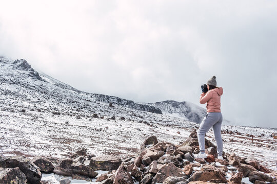 Woman photographer standing on some rocks taking landscape photos on a snowy mountain in the middle of the clouds