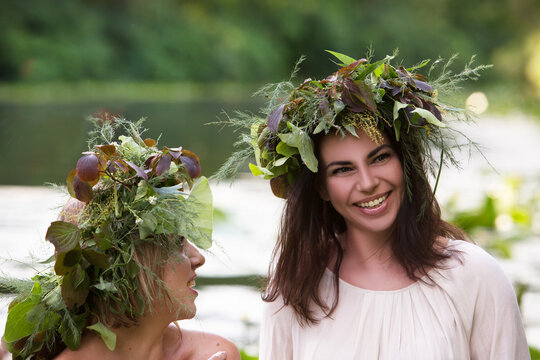 Two happy young women in flower wreaths bathe in a lake with water lilies.