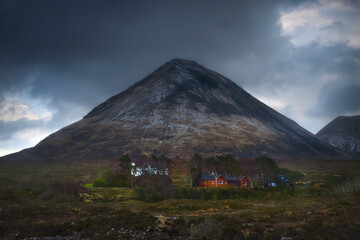Fototapeta premium large triangular shaped mountain in Glen Sligachan with typical wooden huts on the Isle of Skye amongst isolated trees