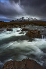 Dramatic sky over large mountains from the River Sligachan on the Isle of Skye Scotland with the Cuillin mountain range in the distance with snow in winter, Isle of Skye, Scotland