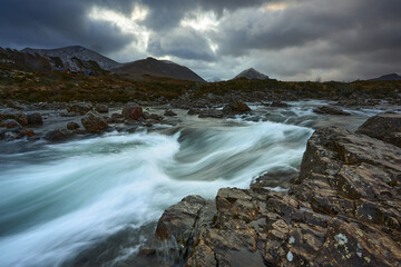 Long exposure of water with rocks in the foreground, winter vegetation on the River Sligachan on the Isle of Skye Scotland with the Cuillin mountain range in the distance, Isle of Skye, Scotland