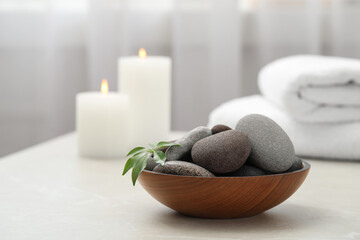 Fototapeta na wymiar Spa stones in wooden bowl on white table indoors