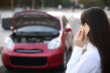 Young woman talking on phone near broken car outdoors