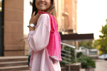 Young woman with stylish pink net bag on city street, closeup