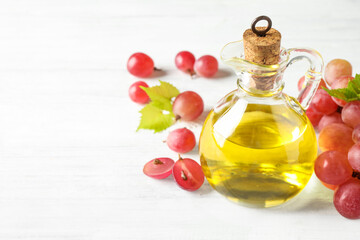Natural grape seed oil and fresh berries on white wooden table, space for text. Organic cosmetic