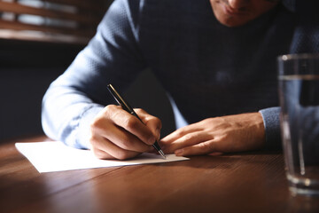 Man writing letter at wooden table indoors, closeup - obrazy, fototapety, plakaty