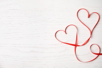 Hearts made of red ribbon on white wooden background, top view with space for text. Valentine's day celebration