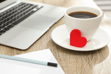 Cup with red heart and laptop on table. Valentine's day celebration