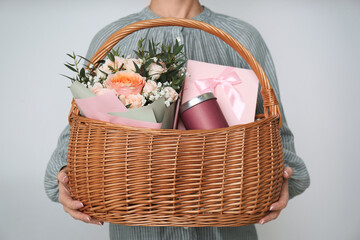 Woman holding wicker basket with different gifts on grey background, closeup