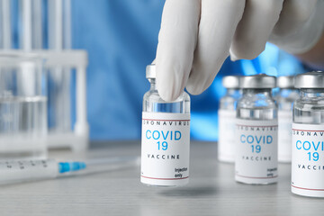 Doctor taking glass vial with COVID-19 vaccine from  table, closeup