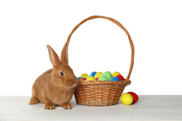 Cute bunny and basket with Easter eggs on table against white background