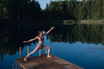 Fototapeta na wymiar Healthy woman practicing yoga on the lake at sunrise enjoying positive energies from nature