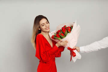 Happy woman receiving red tulip bouquet from man on light grey background. 8th of March celebration