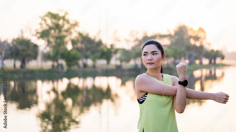 Wall mural Young beautiful Asian woman in sports outfits doing stretching before workout outdoor in the park in the morning to get a healthy lifestyle. Healthy young woman warming up outdoors.