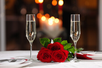 Romantic dinner table setting with glasses of champagne and red roses in restaurant