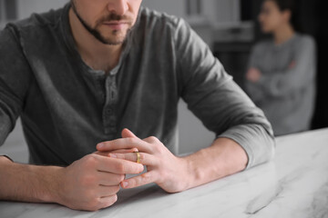 Man taking off wedding ring at white marble table indoors, closeup. Couple on verge of divorce