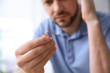Fototapeta premium Man holding wedding ring on light background, closeup. Divorce concept