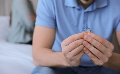 Man with wedding ring in bedroom, closeup. Couple on verge of divorce