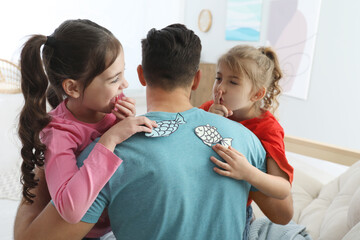 Cute little children sticking paper fish to father's back at home