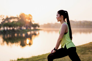 Fototapeta na wymiar A young Asian female workout before a fitness training session at the park under sunlight in the morning. Healthy young woman warming up outdoors. Sport and recreation
