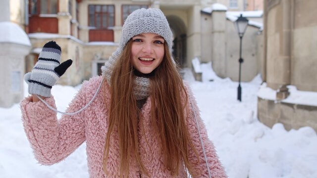 Woman tourist looking to camera, waving hi, hello, welcome, goodbye gesture sign while standing outdoors in winter. Caucasian pretty girl with smile on face posing on street in city. Positive emotions
