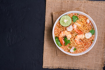 Ramen Instant Noodles in Spicy Shrimp Soup Tom Yum Kung - Asian style food. Placed on a black table with copy space, top view.