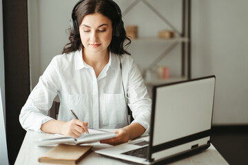 Woman in headphones work on laptop making notes