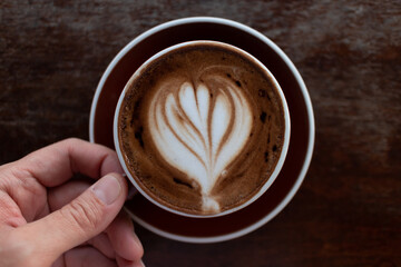 Top view of a hot cup of latte art coffee on dark wooden table.