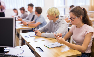 Fototapeta premium Group of focused teenagers using phones at class in auditorium