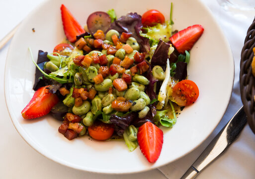 Fresh salad with beans, strawberry, arugula and bacon marinated with soy and honey