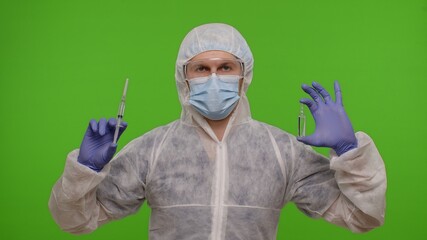 Medical worker doctor in protective PPE suit with vaccine ampoule and syringe in hands offering vaccination against coronavirus covid-19 epidemic. Man isolated on chroma key background. Copy-space